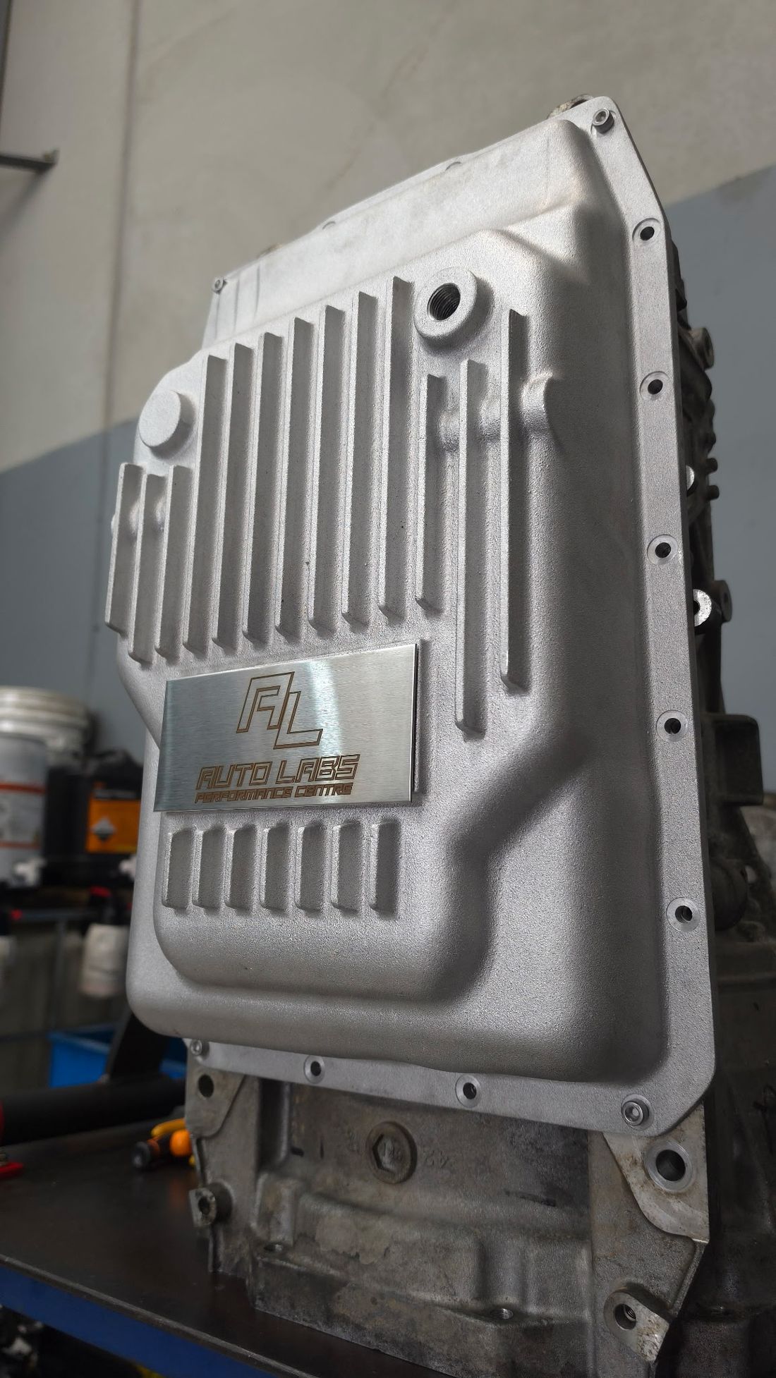 The Auto Labs 10R80 deep cast aluminium transmission pan fitted to a 10-speed transmission on the bench at Pakenham — external cooling fins, temp sender port and etched AL plate